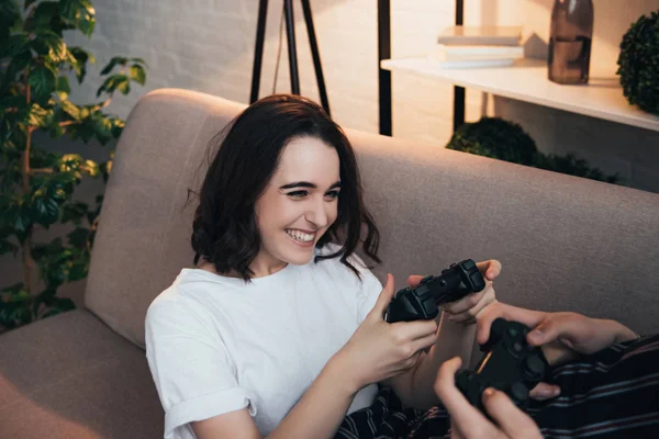 Schöne lächelnde junge Frau sitzt auf der Couch und hält Steuerknüppel mit Mann im Wohnzimmer — Stockfoto