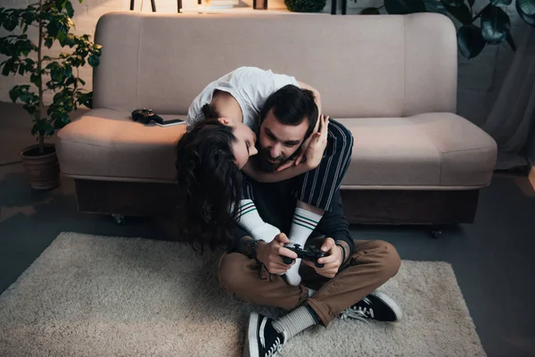 Mulher abraçando e beijando o homem jogando videogame com joystick na sala de estar — Fotografia de Stock