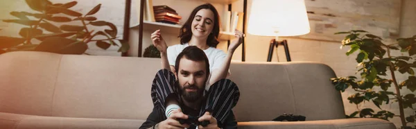 Homme donnant tour de piggyback à belle femme heureuse tout en jouant au jeu vidéo dans le salon — Photo de stock