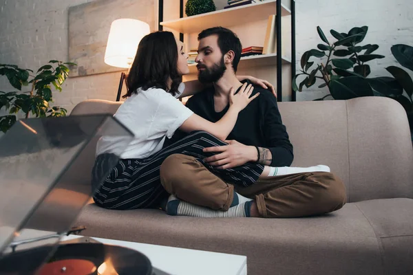 Beautiful young couple sitting on couch and listening to vinyl record in living room — Stock Photo