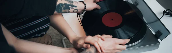 Cropped view of tattooed couple putting vinyl record on record player — Stock Photo