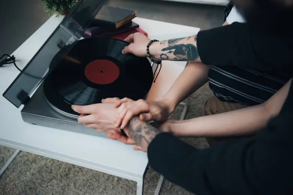 Vista recortada de pareja tatuada poniendo disco de vinilo en el tocadiscos - foto de stock