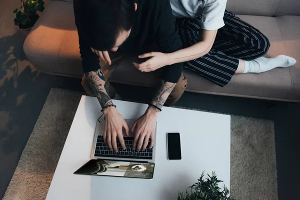 Abgeschnittene Ansicht eines Paares, das sitzt und sich umarmt, während es Laptop mit Buchungswebseite auf dem Bildschirm zu Hause benutzt — Stockfoto