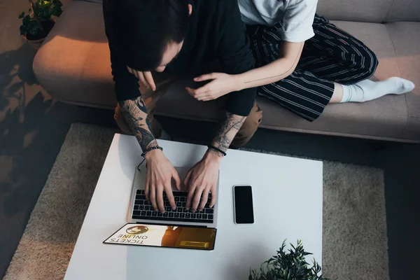 Обрезанный вид пары сидя анг объятия при использовании ноутбука с билетами онлайн сайт на экране дома — стоковое фото