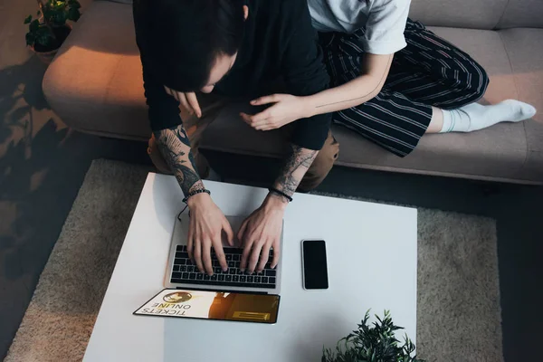 Cropped view of couple sitting ang hugging while using laptop with tickets online website on screen at home — Stock Photo