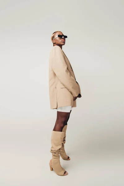 Fashionable african american girl posing in sunglasses and beige jacket isolated on grey — Stock Photo