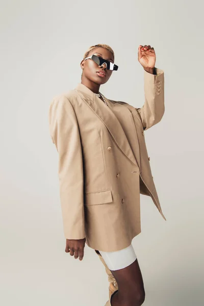 Beautiful african american girl posing in sunglasses and beige jacket isolated on grey — Stock Photo