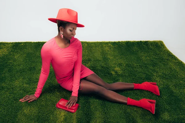 Donna afroamericana in abito rosa e cappello in posa con borsa su erba verde — Foto stock