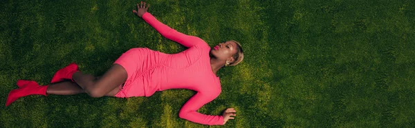 Blick von oben auf eine elegante afrikanisch-amerikanische Frau im rosa Kleid, die auf grünem Gras liegt — Stockfoto