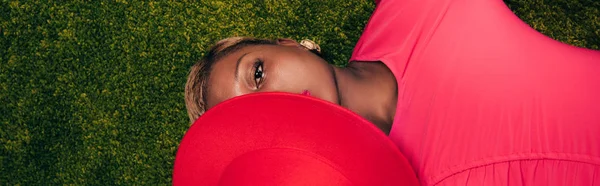 Vue de dessus de la femme afro-américaine aux cheveux courts posant avec chapeau rose sur herbe verte — Photo de stock