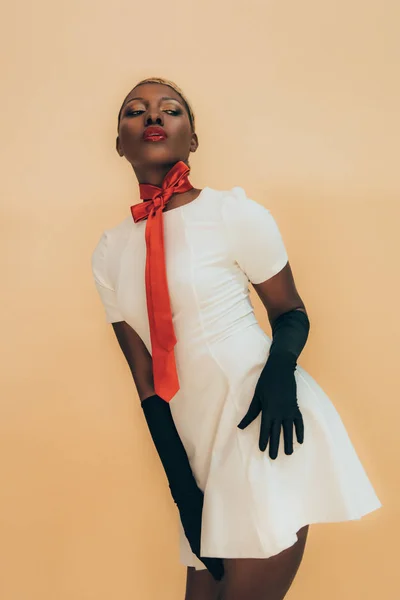 Sensuelle afro-américaine posant en robe blanche, écharpe rouge et gants noirs isolés sur beige — Photo de stock