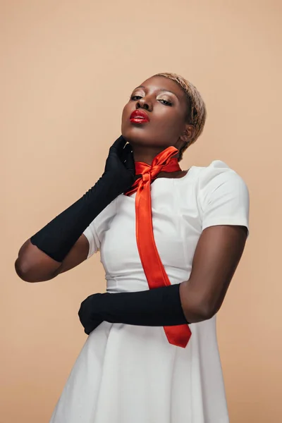 Sexy ragazza afroamericana posa in abito bianco, sciarpa rossa e guanti neri isolati su beige — Foto stock