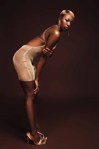 Mujer afroamericana de moda con el pelo corto posando en vestido glamoroso en marrón - foto de stock