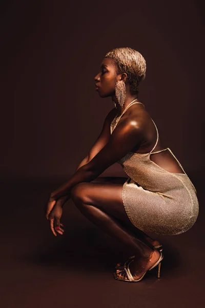 Side view of african american woman with short hair posing in glamorous dress on brown — Stock Photo