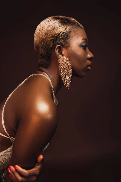 Vista lateral de la atractiva mujer afroamericana con el pelo corto aislado en marrón - foto de stock