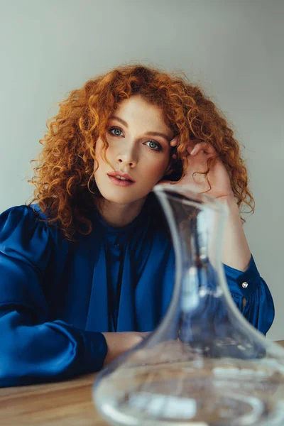 Bela mulher ruiva elegante posando perto vaso de vidro isolado no cinza — Fotografia de Stock