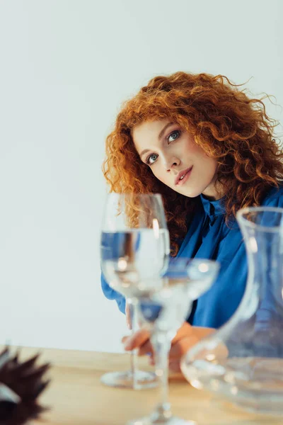 Attrayant élégant rousse femme posant près de la table avec des verres d'eau isolé sur gris — Photo de stock