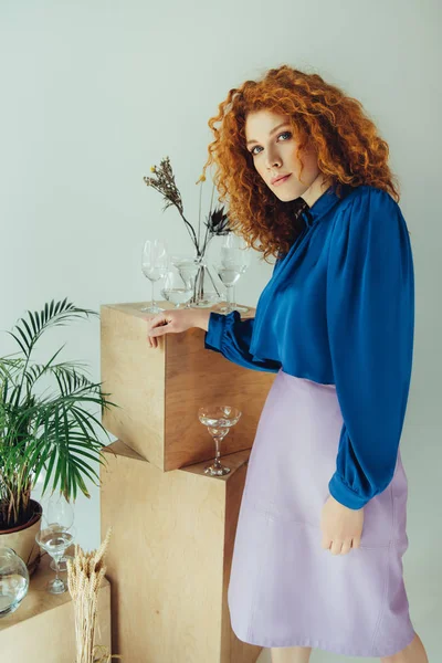 Stylish attractive redhead girl posing near wooden boxes with glasses and dried flowers on grey — Stock Photo