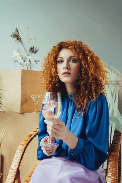 Hermosa mujer pelirroja elegante sosteniendo vidrio con flor - foto de stock