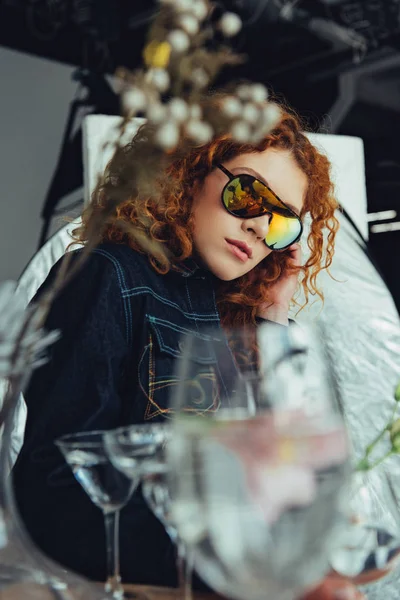 Selective focus of stylish redhead woman in sunglasses posing near glasses and dried flowers — Stock Photo