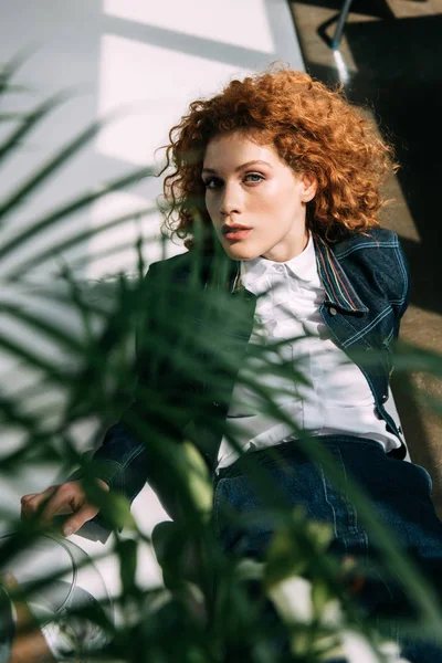 Selective focus of stylish redhead girl posing near green leaves — Stock Photo