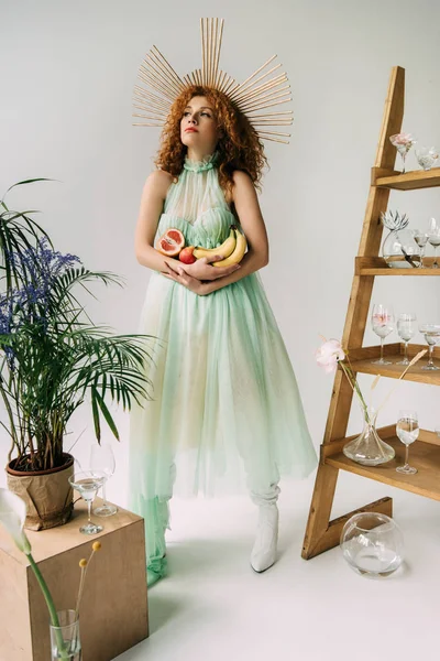 Стильная девушка с аксессуаром на голове и фруктами возле лестницы с цветами и очками — стоковое фото