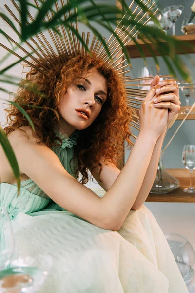 Fashionable redhead girl with accessory on head in dress posing near plant — Stock Photo