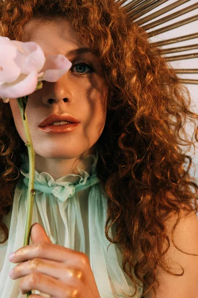 Beautiful redhead girl with accessory on head posing with flower and looking at camera — Stock Photo