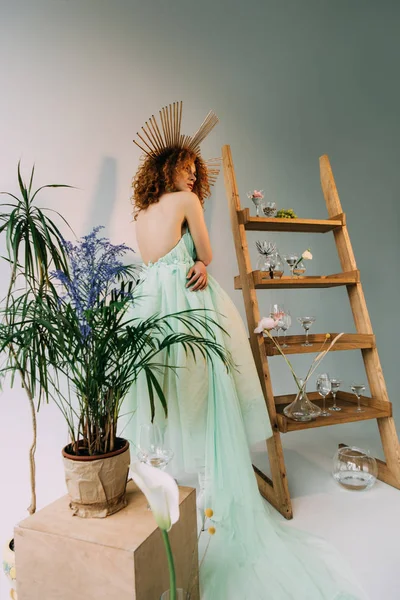 Fashionable redhead girl with accessory on head posing near ladder with flowers and glasses — Stock Photo