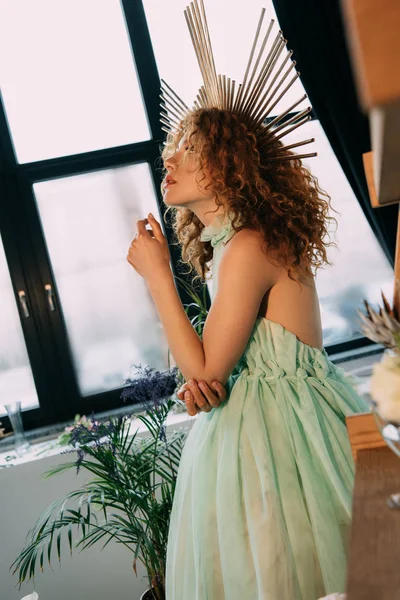 Beautiful stylish redhead girl with accessory on head in dress near plant — Stock Photo