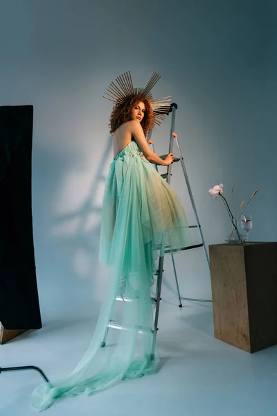 Beautiful stylish girl with accessory on head posing on ladder and looking at camera — Stock Photo