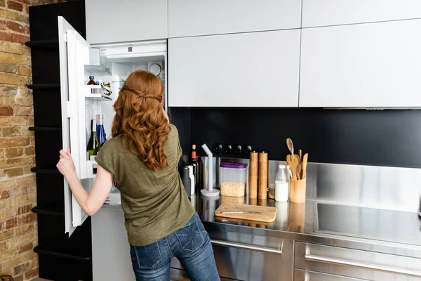 Vue arrière de la femme debout près d'un réfrigérateur ouvert dans la cuisine — Photo de stock