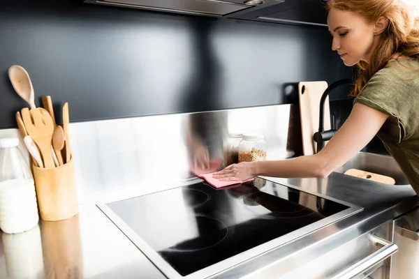 Attractive woman cleaning stove with rag in kitchen — Stock Photo