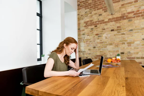 Freelancer atraente segurando documento perto de dispositivos digitais na mesa em casa — Fotografia de Stock