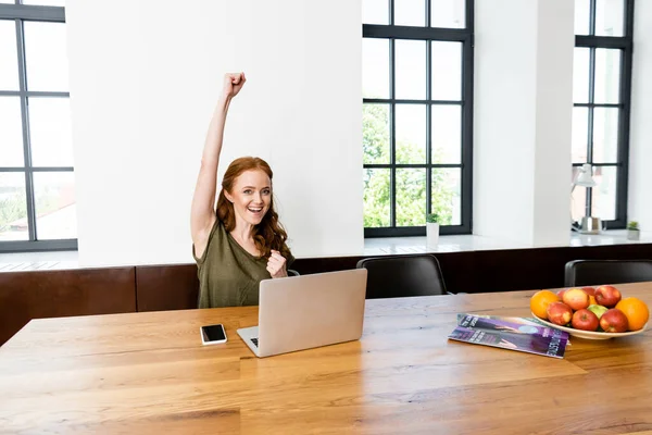 Freelancer sonriente mostrando sí gesto cerca de la computadora portátil y el teléfono inteligente en la mesa - foto de stock