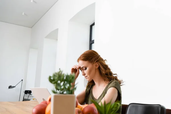 Selective focus of sad freelancer using laptop near fruits and plants on table — Stock Photo