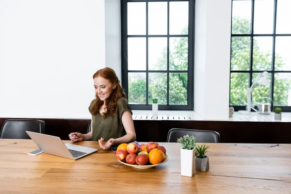 Позитивний співробітник має відеодзвінок на ноутбук біля фруктів і рослин на столі — стокове фото