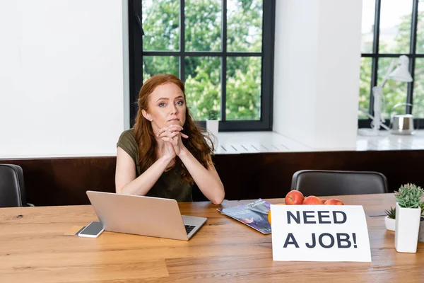 Freelancer mirando a la cámara cerca de gadgets, tarjeta de crédito y tarjeta con necesidad de un trabajo de letras en casa — Stock Photo