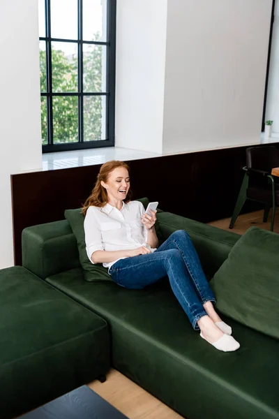 Смеющаяся женщина с ноутбука, сидя на диване в гостиной — стоковое фото