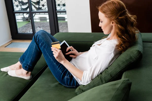 Vue latérale de la femme utilisant une tablette numérique et une carte de crédit sur le canapé — Photo de stock