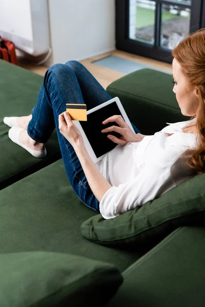 Focus selettivo della donna in possesso di carta di credito e utilizzando tablet digitale con schermo bianco a casa — Foto stock