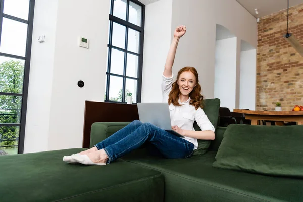 Femme positive montrant un geste oui tout en tenant un ordinateur portable sur le canapé — Photo de stock