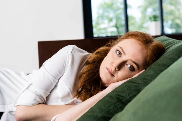 Selective focus of sad woman looking at camera while lying on sofa at home — Stock Photo