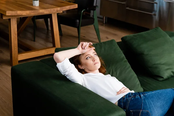 Mujer decepcionada con la mano cerca de la frente acostada en el sofá en casa - foto de stock