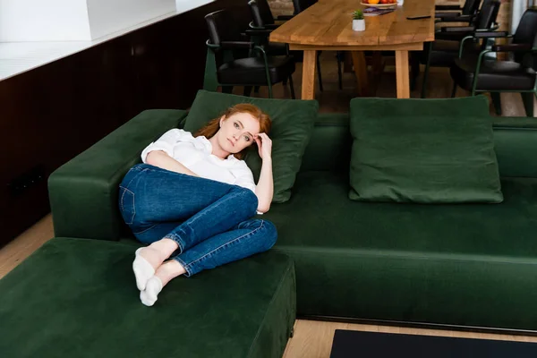 Donna triste guardando la fotocamera mentre sdraiato sul divano a casa — Foto stock
