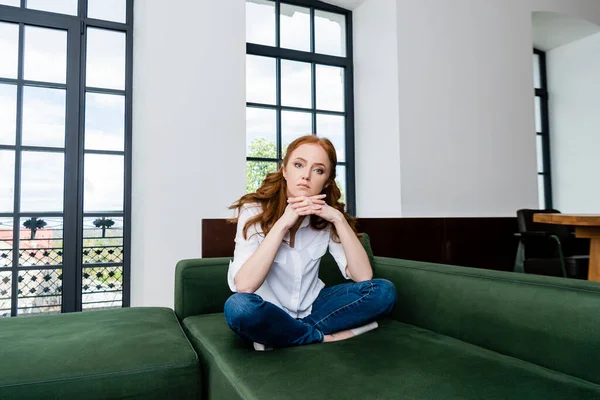 Schöne Frau mit geballten Händen, die auf dem Sofa im Wohnzimmer in die Kamera schaut — Stockfoto