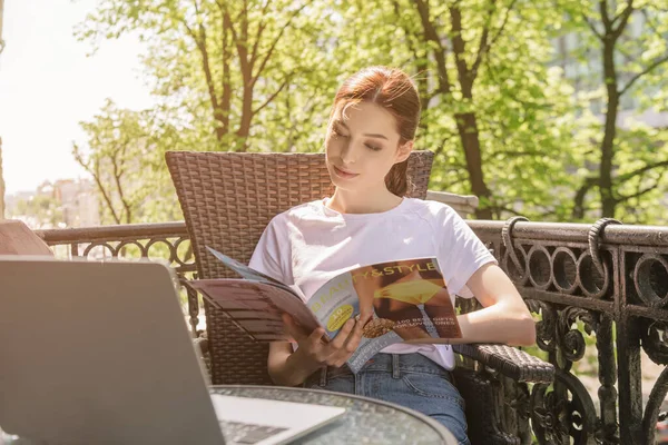 Bastante freelancer revista de lectura cerca del ordenador portátil en la mesa - foto de stock