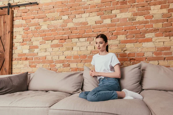 Jovem mulher atraente sentado no sofá com travesseiros macios — Fotografia de Stock