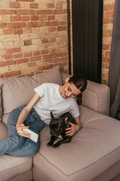Allegro giovane donna prendendo selfie con carino bulldog francese in soggiorno — Foto stock