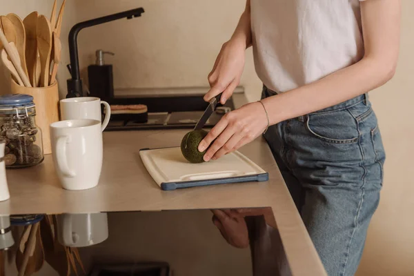 Abgeschnittene Ansicht einer Frau, die leckere Avocado in der Nähe von Tassen schneidet — Stockfoto